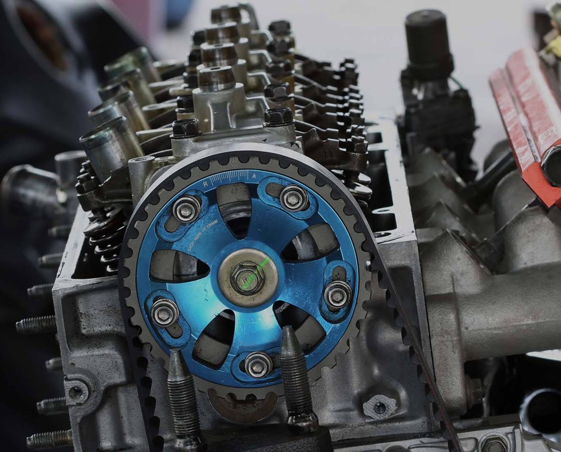 A cylinder head on the bench at A & C Automotive, mid-rebuild, with the timing gear and fuel rail exposed